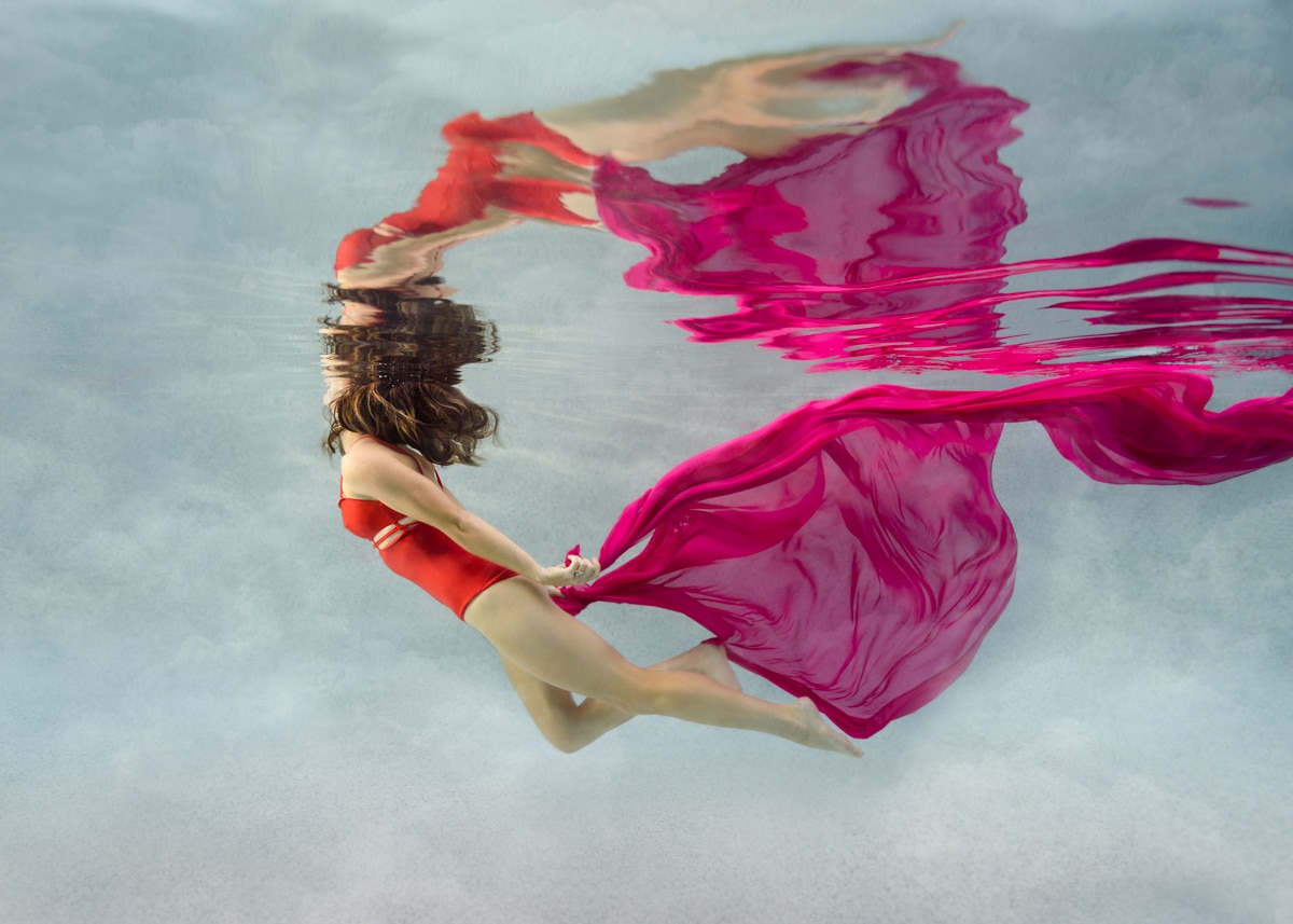 woman swimming underwater, clouds background, water reflections, pink chiffon flowing fabric